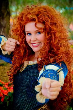 a woman with long red hair pointing to the side and smiling while wearing a blue dress