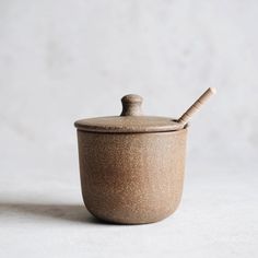 a brown ceramic container with a wooden spoon in the lid on a white tablecloth