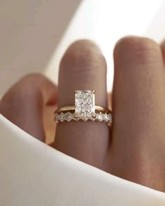 a woman's hand with a diamond ring on top of her finger and white cloth in the background