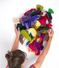 a woman is reaching up towards a pile of multicolored hair clips on a white background