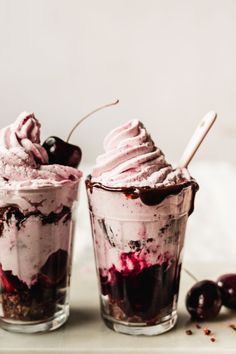 two glasses filled with ice cream and cherries on a table next to each other