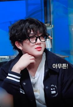 a young man with glasses sitting in front of a blue wall