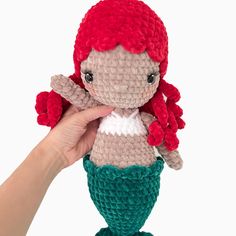 a crocheted little mermaid doll is held up to the camera by someone's hand