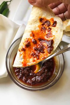 a hand holding a spoon over a bowl filled with chili and cheese quesadilla