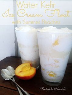 two glasses filled with ice cream and peaches next to spoons on a table