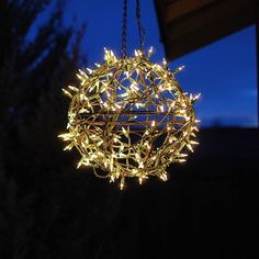 a lighted ball hanging from a chain in the night sky with trees and bushes behind it