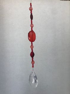 a red glass beaded wind chime hanging from a hook on a white wall