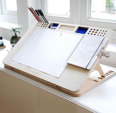 a white desk with a pen, notebook and pencils on it in front of a window