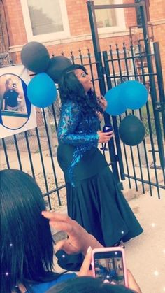 a woman standing in front of a gate with balloons on her head and cell phone