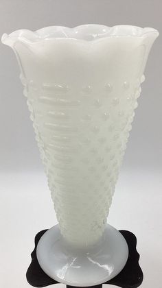 a white glass vase sitting on top of a black and white stand with a circular base