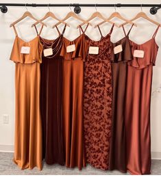 four dresses hanging on a rack in front of a wall with hangers and tags