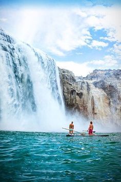 two people are paddling in front of a waterfall