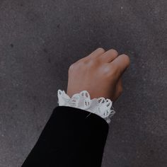 a person's hand wearing a white lace cuff on top of their black jacket