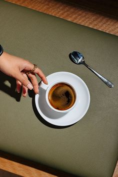 a cup of coffee is being held by someone's hand on a table with spoons