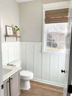 a white toilet sitting in a bathroom next to a window with blinds on the windowsill