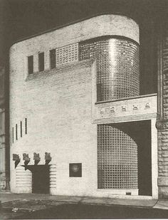 black and white photograph of an old building on the corner of a street in front of a brick wall