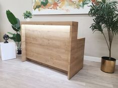 a wooden reception desk next to two potted plants and a painting on the wall