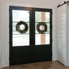 two wreaths on the front doors of a house with wood floors and white walls