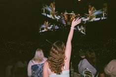 a group of people at a concert with their arms in the air and one person holding up her hand