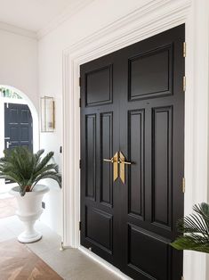 a black front door with gold handles and two planters on the floor in front of it