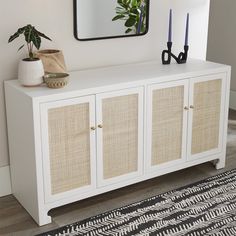 a white sideboard with wicker doors and two blue candles on top next to a mirror