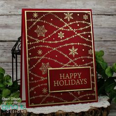 a red and gold holiday card with snowflakes on it, sitting next to some green leaves