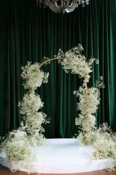 an arch made out of branches and flowers on a stage with green curtains behind it