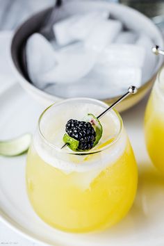 two glasses filled with lemonade and blackberries sitting on a plate next to an ice bucket