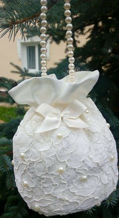 a white ornament hanging from a christmas tree with pearls and bows on it