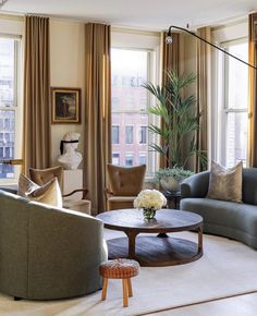 a living room filled with lots of furniture next to tall windows and curtains on the window sill