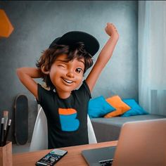 a young boy sitting at a desk in front of a laptop computer with his arms up