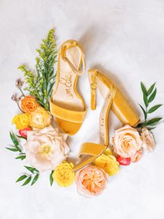 a pair of yellow high heeled shoes surrounded by flowers and greenery on a white background