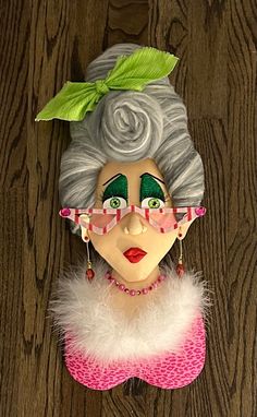 a doll with glasses and a green leaf on it's head is hanging from a wooden wall