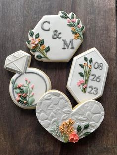 three decorated cookies on top of a wooden table with initials and flowers in the shape of hearts