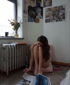 a woman sitting on the floor reading a book in front of a radiator