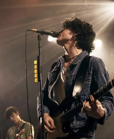 a man singing into a microphone while holding a guitar in front of him on stage