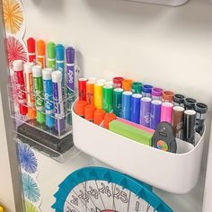 an organized desk with markers, pens and scissors on it in a white container next to a clock