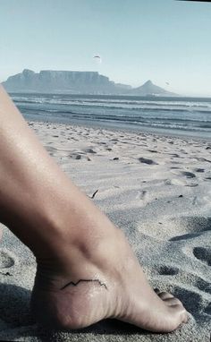 a person's bare foot on the beach with mountains in the backgroud