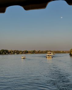 two boats are traveling down the river in front of some trees and a moon above them