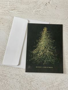 a card with a christmas tree on it next to a white envelope that says merry christmas