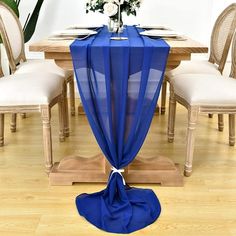 a blue table cloth draped over a wooden dining room table with white chairs and flowers on it