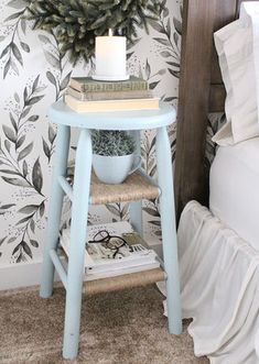 a small blue table with a candle and some books on it next to a bed