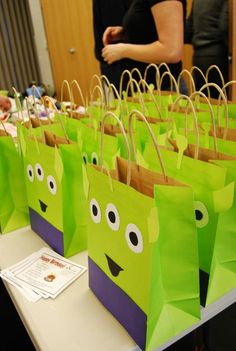 green paper bags with faces on them are sitting on a table while people stand in the background