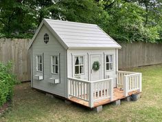 a small gray house sitting on top of a wooden platform in the grass next to a fence