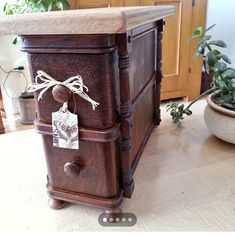 an old wooden box with a tag tied to it on a table next to potted plants