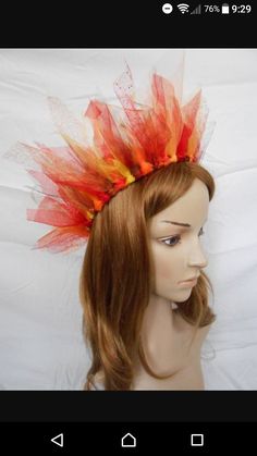 a woman's headpiece with red and orange feathers on it, sitting on top of a mannequin