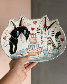 a hand holding a plate with two cats on it and a cake in the middle