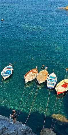 several small boats tied up to the rocks by ropes in clear blue water with people standing near them