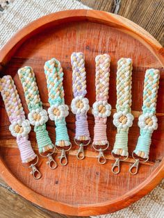 five different colored key chains are on a wooden platter, with flowers and beads attached to them