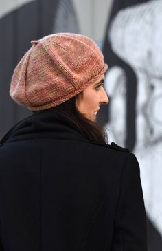 a woman wearing a pink hat and black coat standing in front of a graffiti covered wall